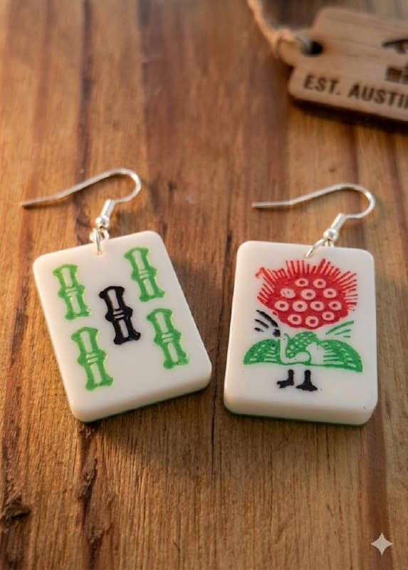Gamenight Mahjong Tile Earrings — deliberately mismatched pair of 3D-printed ivory resin tiles, one with green bamboo stalks and one with the hand-illustrated ‘one bamboo’ bird beneath a red bloom