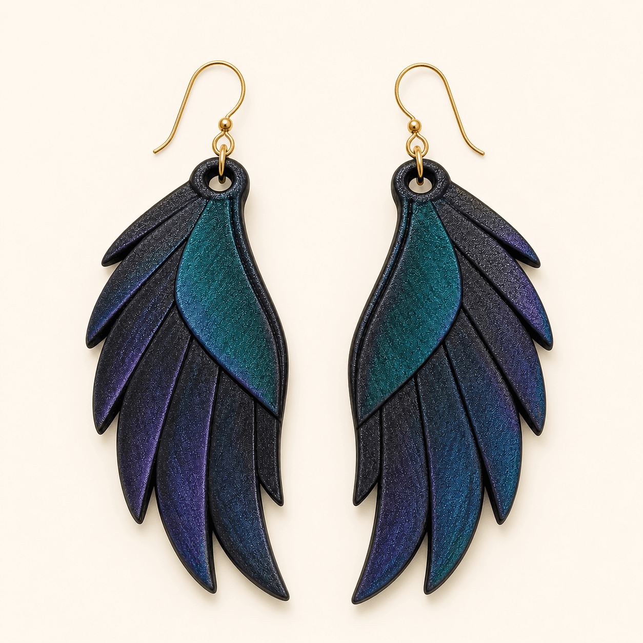 Grackle Wing Earrings — 3D-printed iridescent wing-shaped resin earrings on gold-tone ear wires, with a multi-chrome finish shifting from deep purple to teal green like a grackle’s feathers in the Texas sun