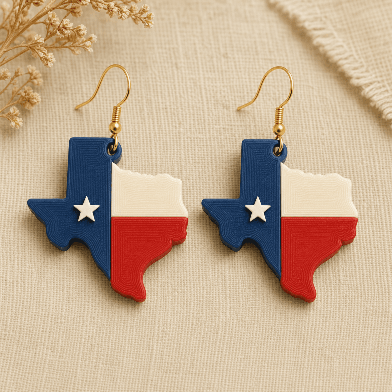 Red, White & Blue Texas Earrings — 3D-printed resin Texas silhouettes color-blocked like the state flag, deep blue with a raised white star beside cream and red panels, on gold-tone ear wires threaded directly through the Panhandle